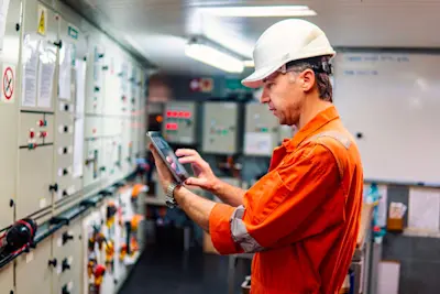 Person in boiler suit and hard hat with a tablet.